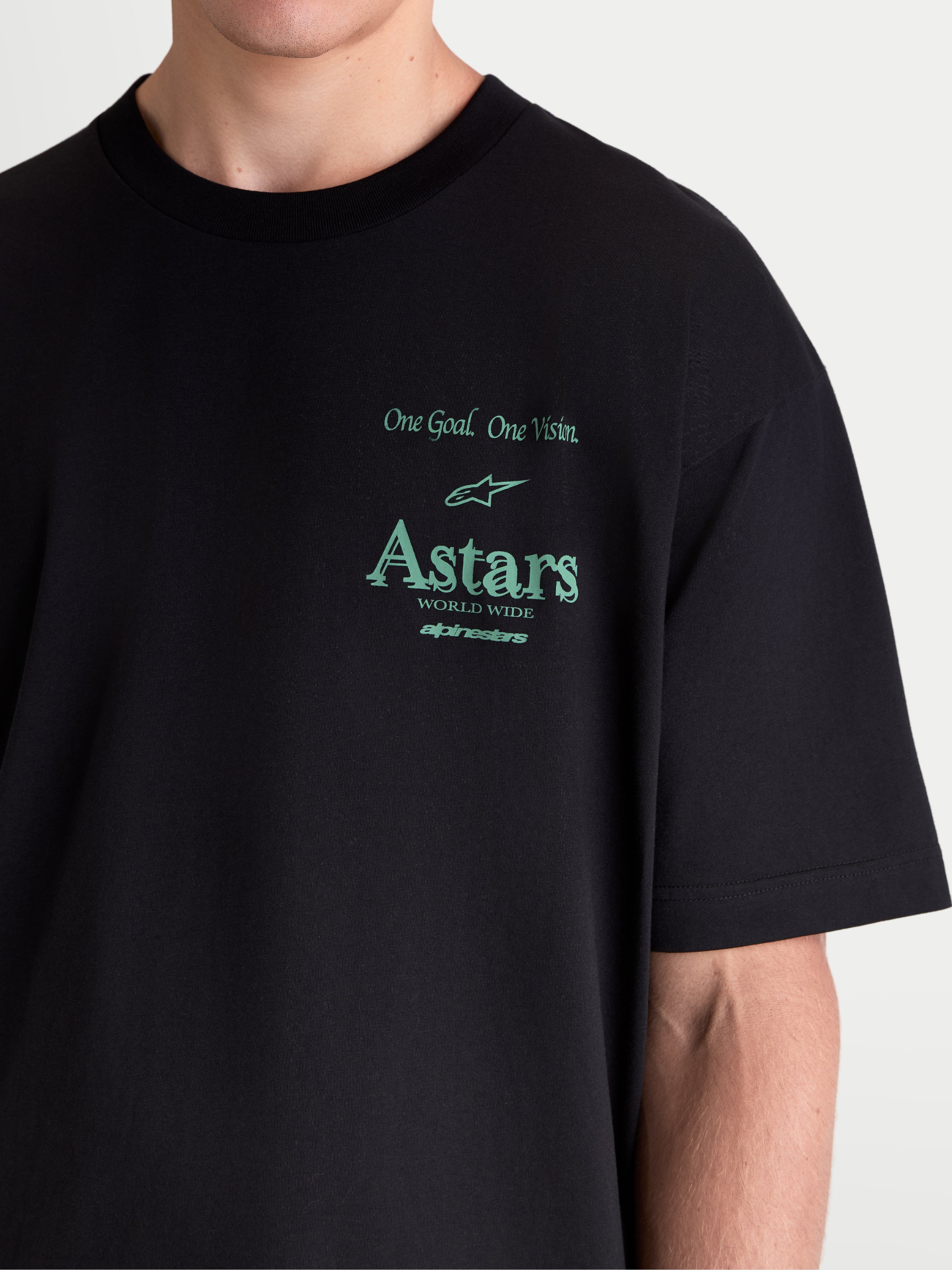Alpinestars T-Shirt Post Oversized CSF, t-shirt de manga curta de sportswear, preta com gráficos em verde, apresentando a frase 'One Goal. One Vision.' e branding Astars, grande plano no modelo mostrando o corte oversized e construção em mistura de algodão premium.