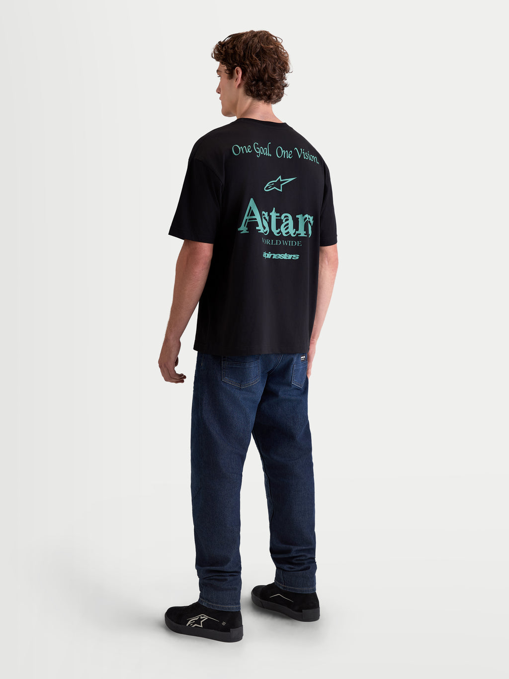 Alpinestars T-Shirt Post Oversized CSF, t-shirt de manga curta para homem, preta com gráficos em verde azulado na parte traseira, vista de costas num modelo, inclui o logótipo Astars e o texto One Goal One Vision e Astars Worldwide, estilo casual sportswear oversized.