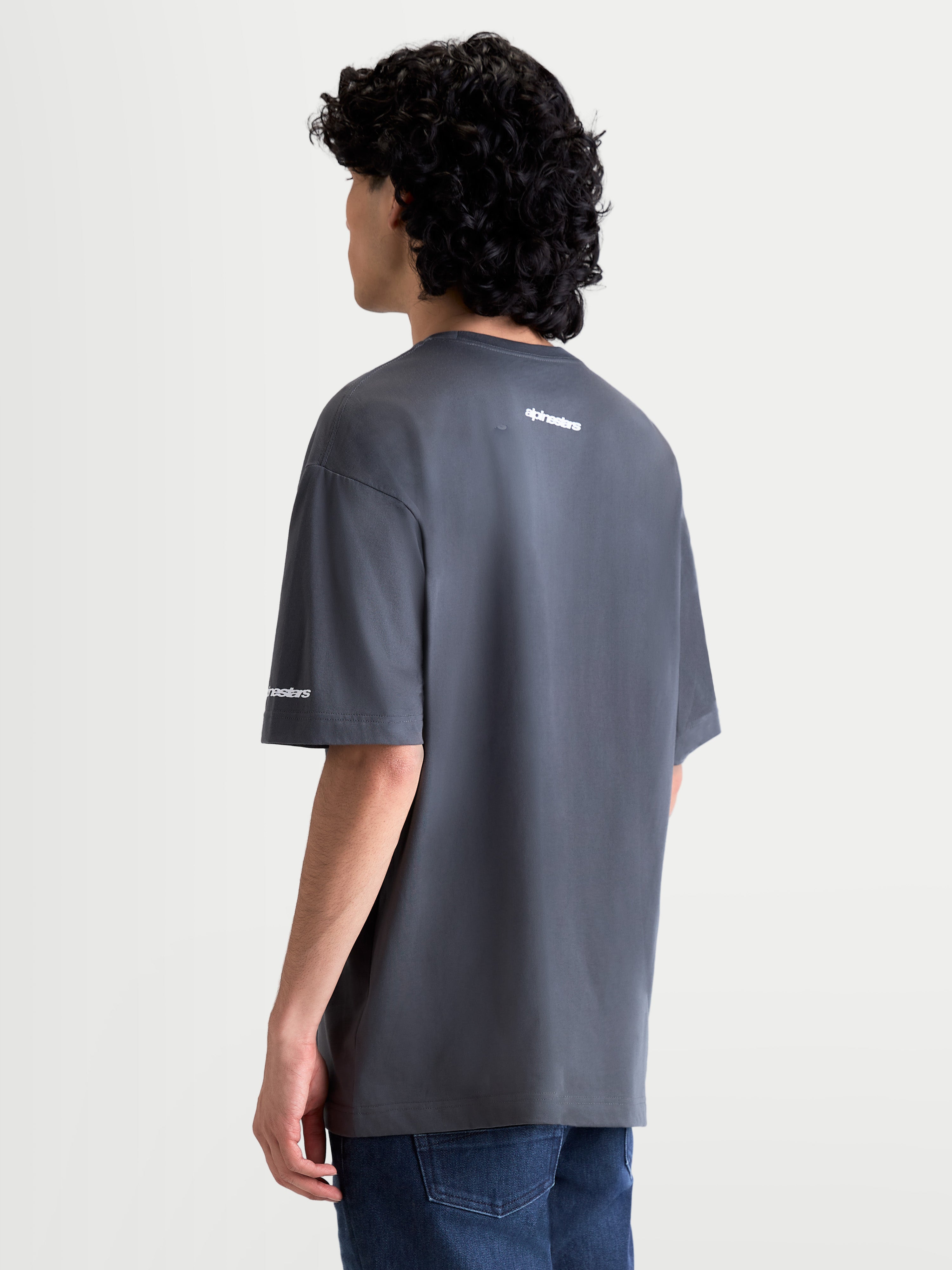 Alpinestars T-Shirt Mandate Oversized CSF, t-shirt de manga curta para homem, cinzenta, vista traseira num modelo, logótipo Alpinestars em relevo branco nas costas e na manga, ajuste oversized, casual sportswear.