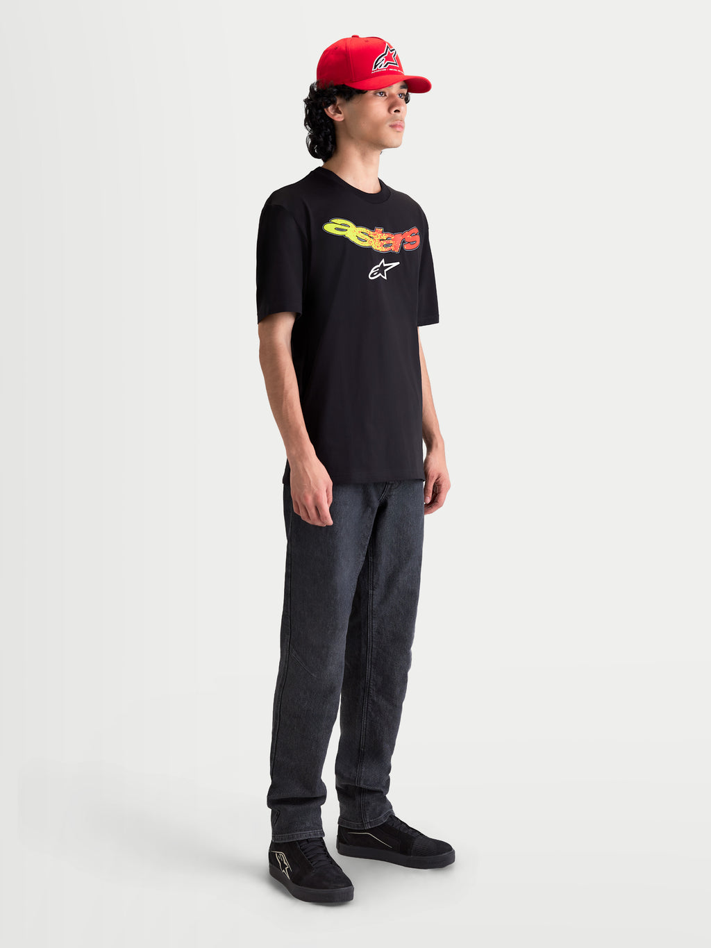 Alpinestars T-shirt Elliptogrit CSF, t-shirt de manga curta para homem, preta com lettering Astars em gradiente amarelo e vermelho e logótipo branco, casual sportswear, modelo a usar a t-shirt.