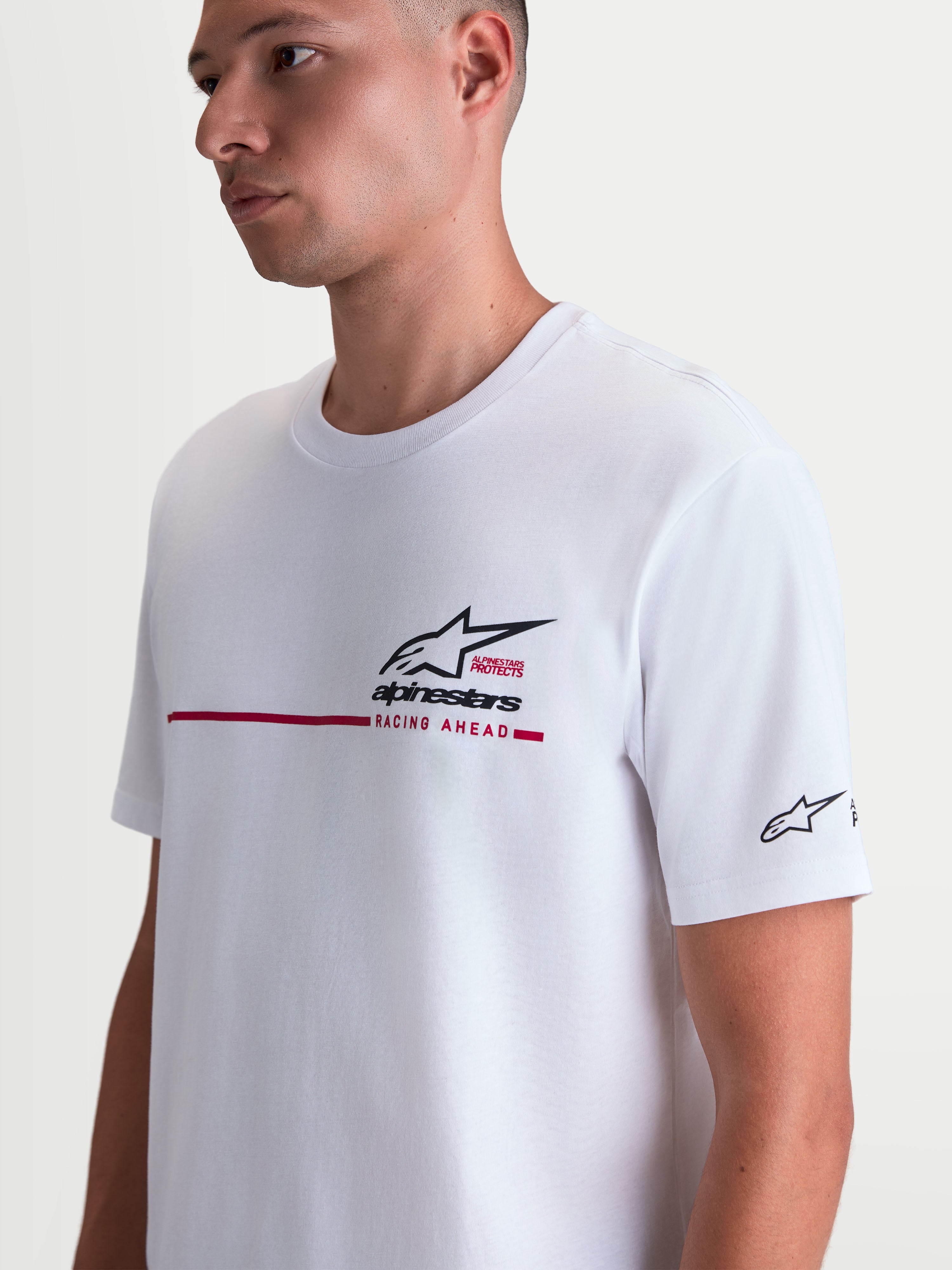 Alpinestars T-Shirt P1 CSF, t-shirt de manga curta unissexo, branca com gráfico de logótipo Astars e faixa de corrida em preto e vermelho, mistura de algodão e poliéster, modelo a usar o artigo.