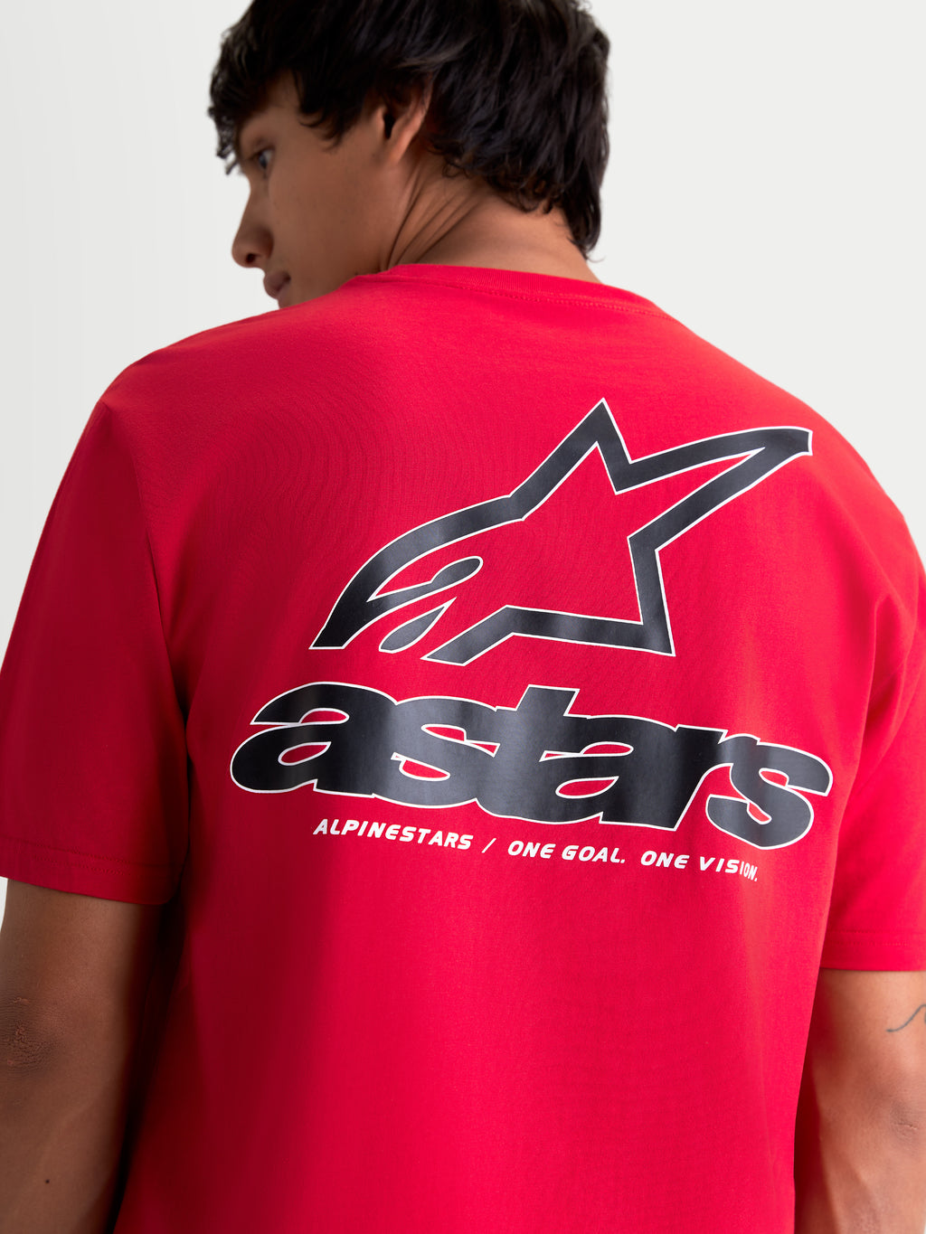Alpinestars T-shirt Lineout CSF, t-shirt de manga curta de sportswear, vermelha com gráficos pretos e brancos, vista traseira no modelo com logótipo Astars grande e o slogan 'One Goal. One Vision.', acabamento de impressão suave ao toque.