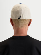 Alpinestars County Canvas Boné, boné desportivo casual, vista traseira num modelo a mostrar o ajuste flex-back e o logótipo subtil na parte traseira, areia e azul, em tecido oxford peached