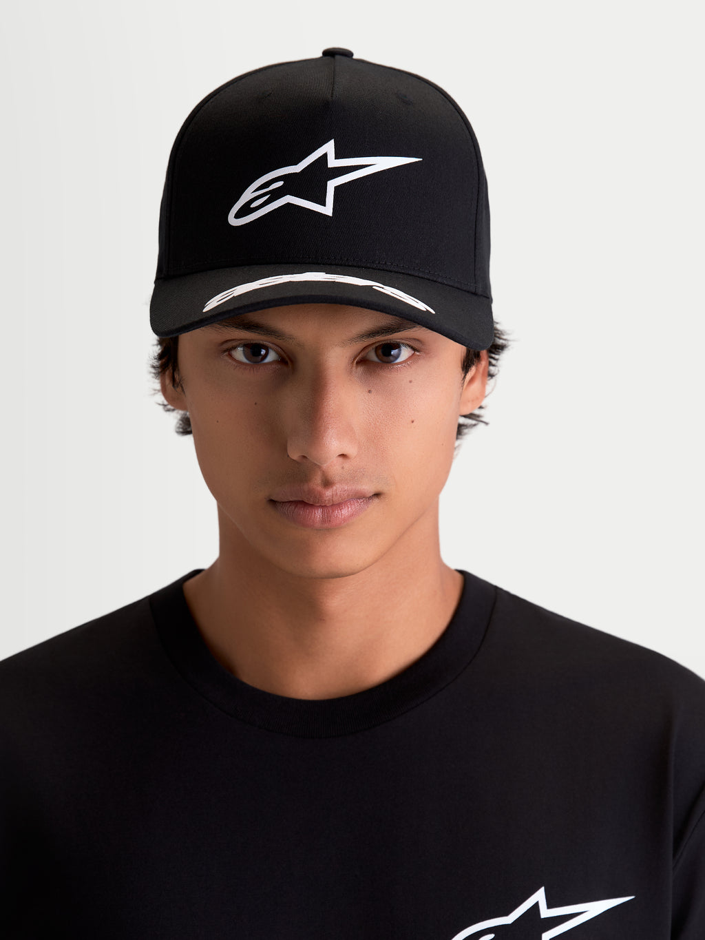 Alpinestars Chapéu Arclight, boné de motorsport sportswear, preto e branco, vista frontal no modelo, logótipo Astars branco em relevo na copa estruturada, aba curva com pormenores e tecido de sarja premium.