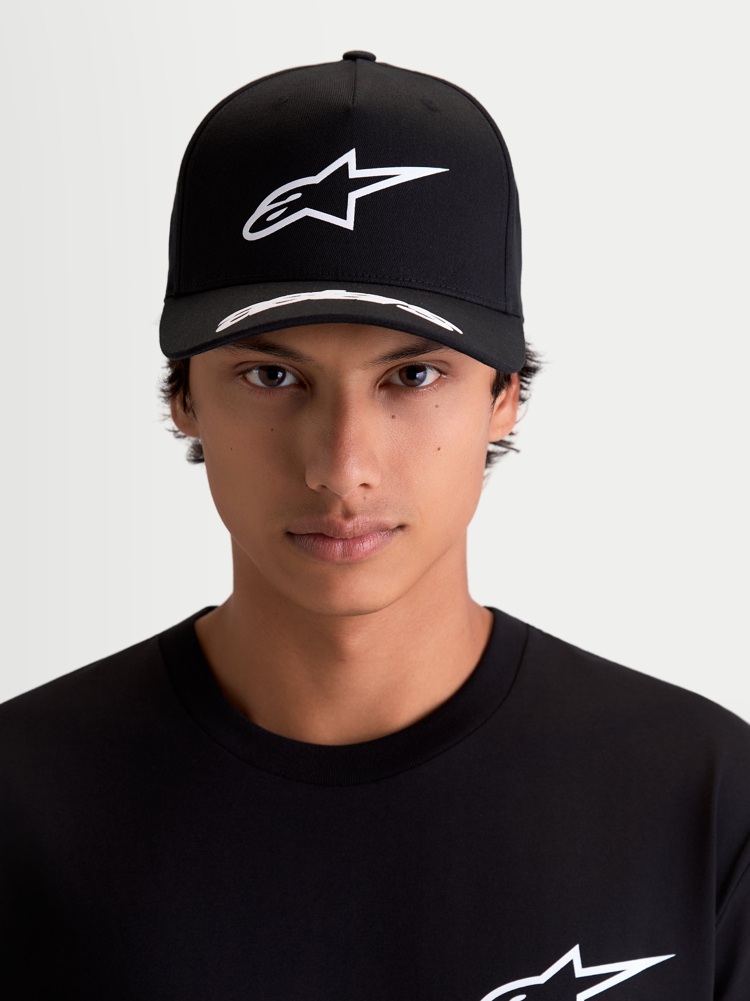 Alpinestars Chapéu Arclight, boné de motorsport sportswear, preto e branco, vista frontal no modelo, logótipo Astars branco em relevo na copa estruturada, aba curva com pormenores e tecido de sarja premium.