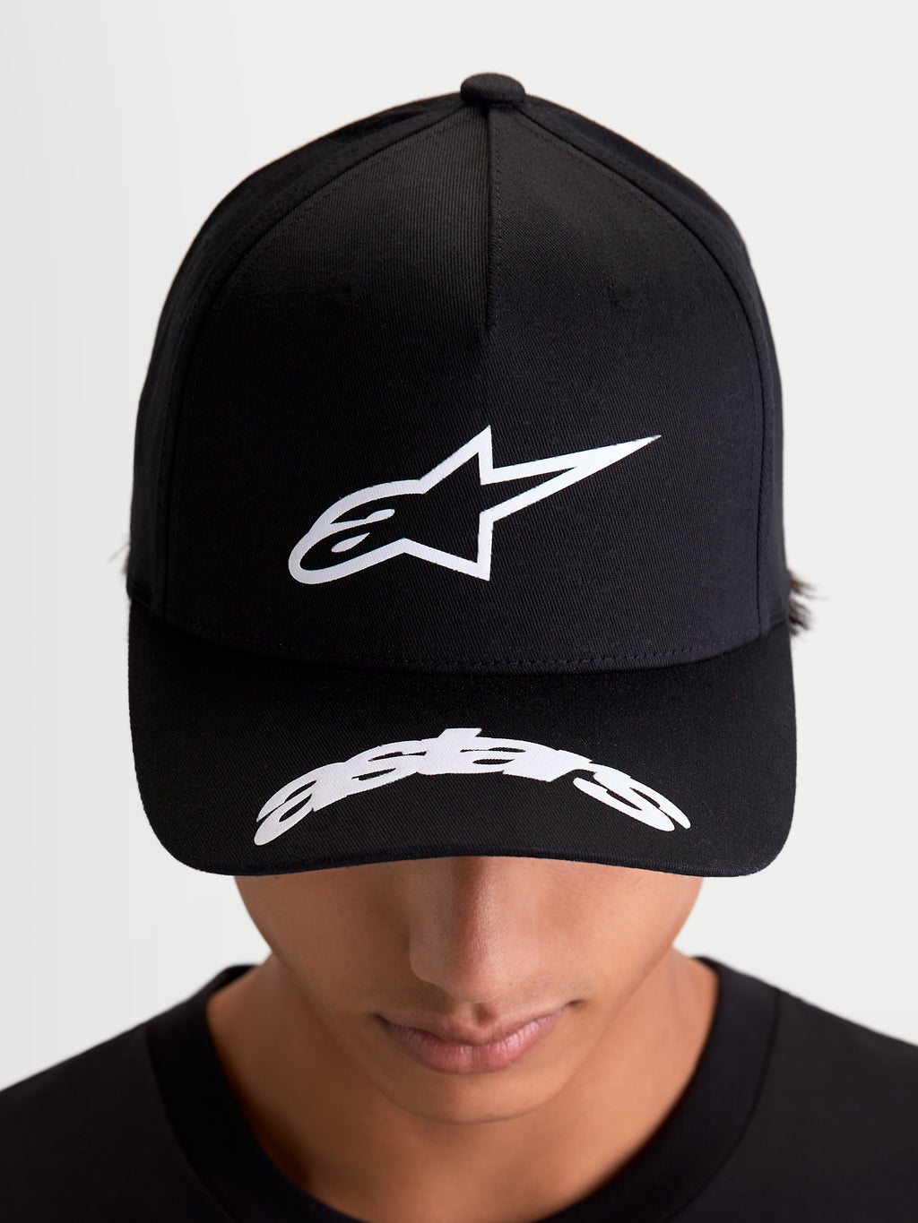 Alpinestars Chapéu Arclight, boné sportswear preto e branco, vista frontal num modelo, com logótipo Astars em relevo na copa estruturada e logótipo curvo na aba, estilo casual inspirado no motorsport