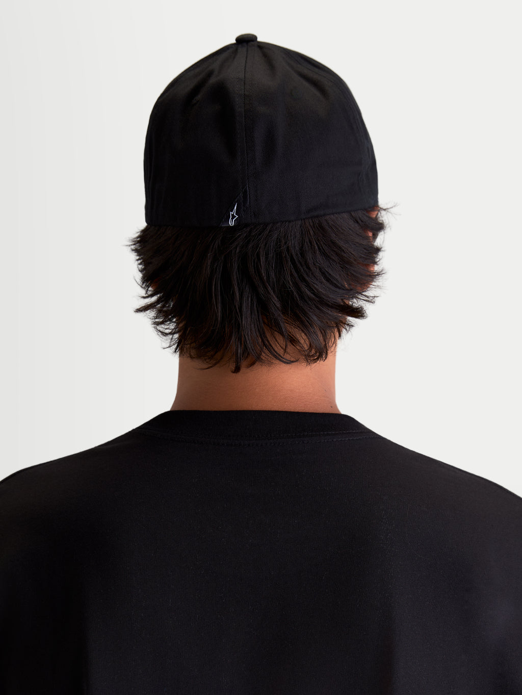 Alpinestars Chapéu Arclight, boné de sportswear preto, vista traseira num modelo, apresentando um pequeno logótipo Astars branco na parte de trás, copa estruturada e construção flexível, em sarja de algodão resistente para conforto diário.