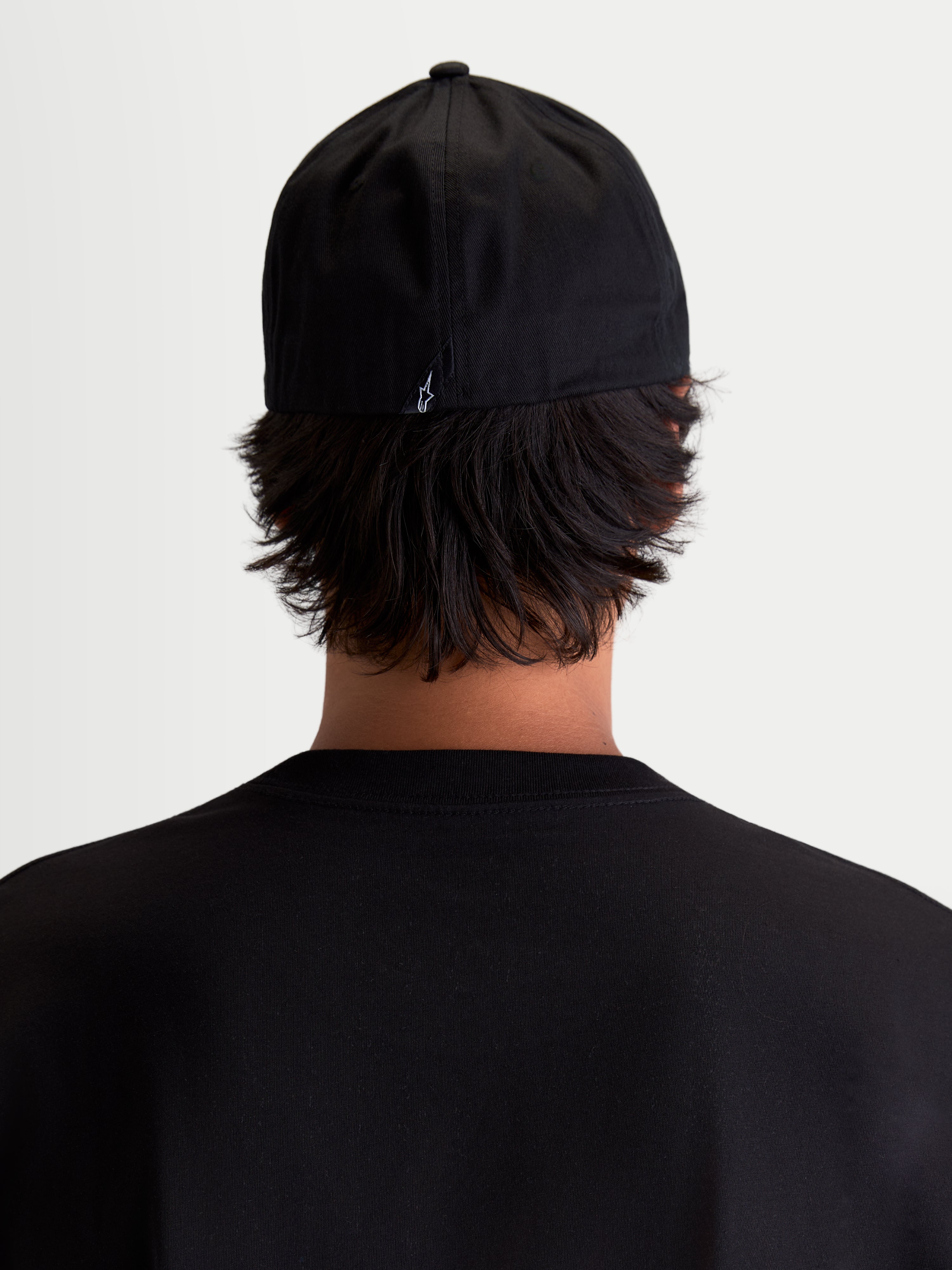 Alpinestars Chapéu Arclight, boné de sportswear preto, vista traseira num modelo, apresentando um pequeno logótipo Astars branco na parte de trás, copa estruturada e construção flexível, em sarja de algodão resistente para conforto diário.