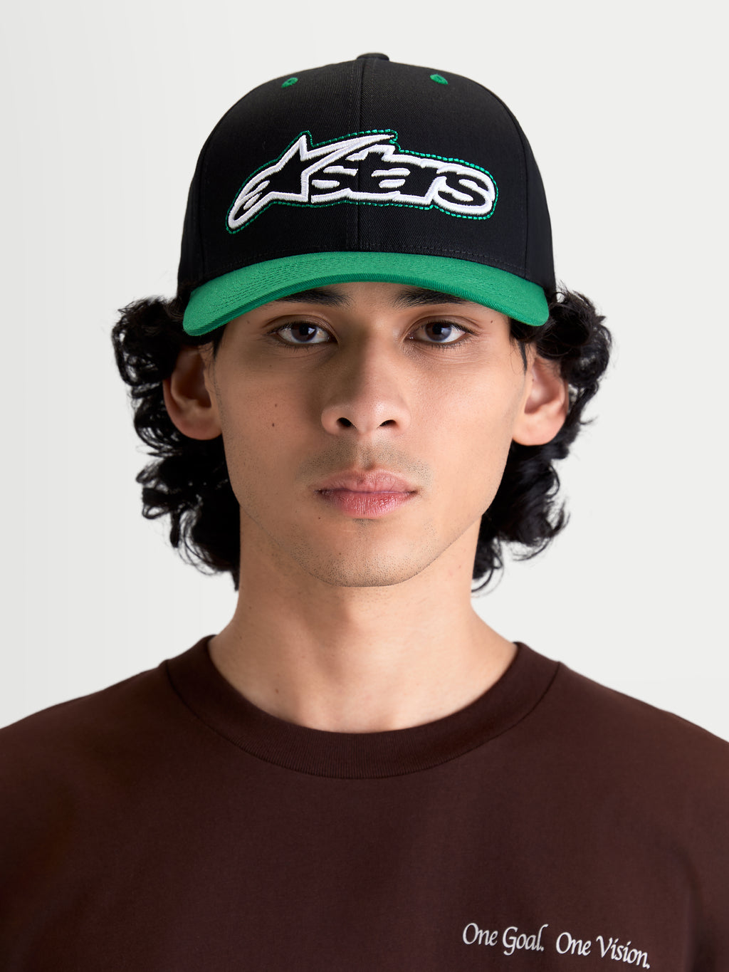 Alpinestars Retro Snapback Hat, Sportswear Lifestyle Cap, Black and Green, featuring a curved bill, structured crown, and front embroidered Astars logo with green running stitch, shown on model front view.