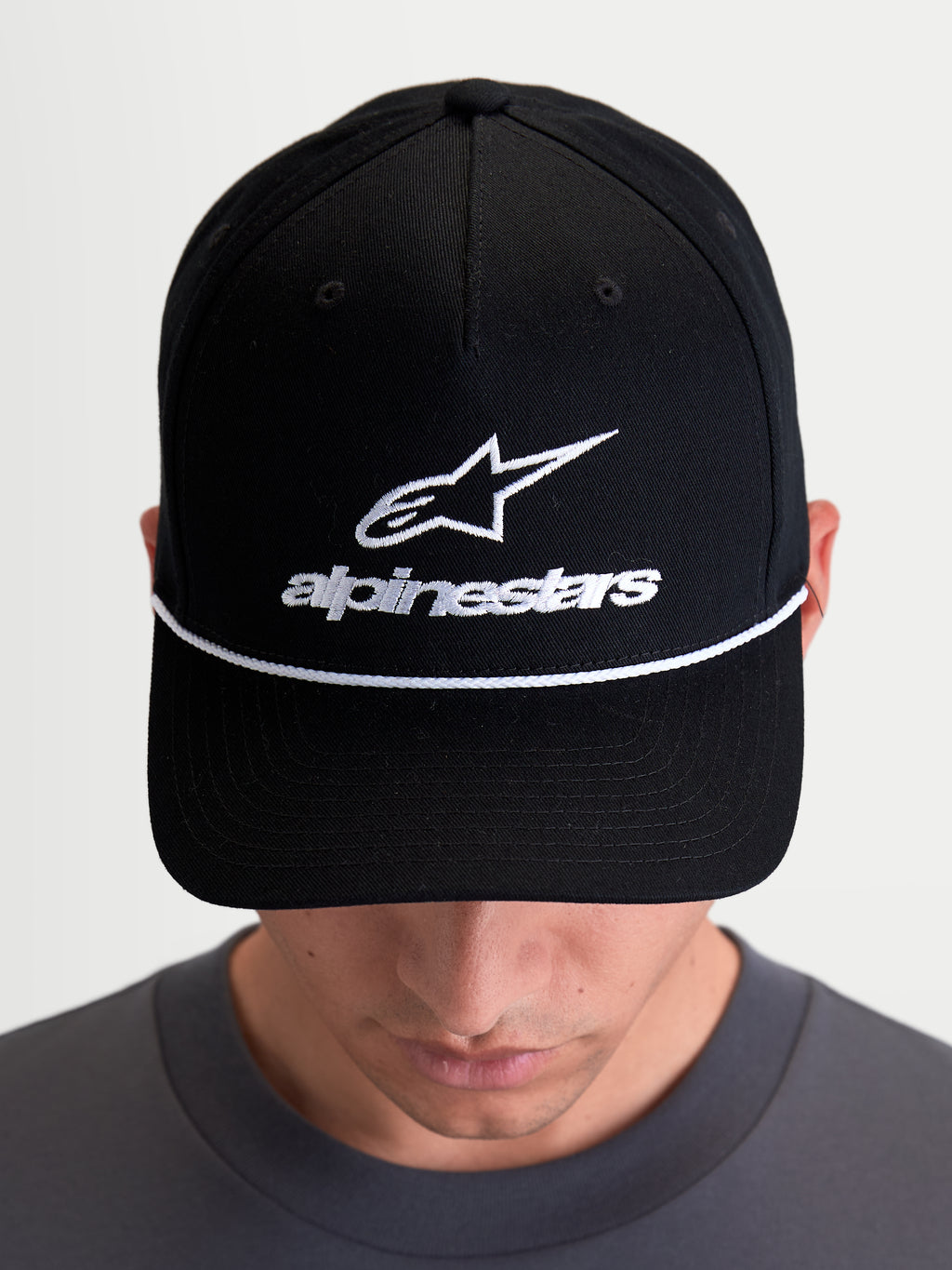 Alpinestars Boné Combo Logo Snapback, boné de sportswear casual unissexo, preto e branco, com logótipo Astars bordado e corda decorativa branca, aba curva e coroa estruturada em sarja de algodão, modelo a usar o artigo.