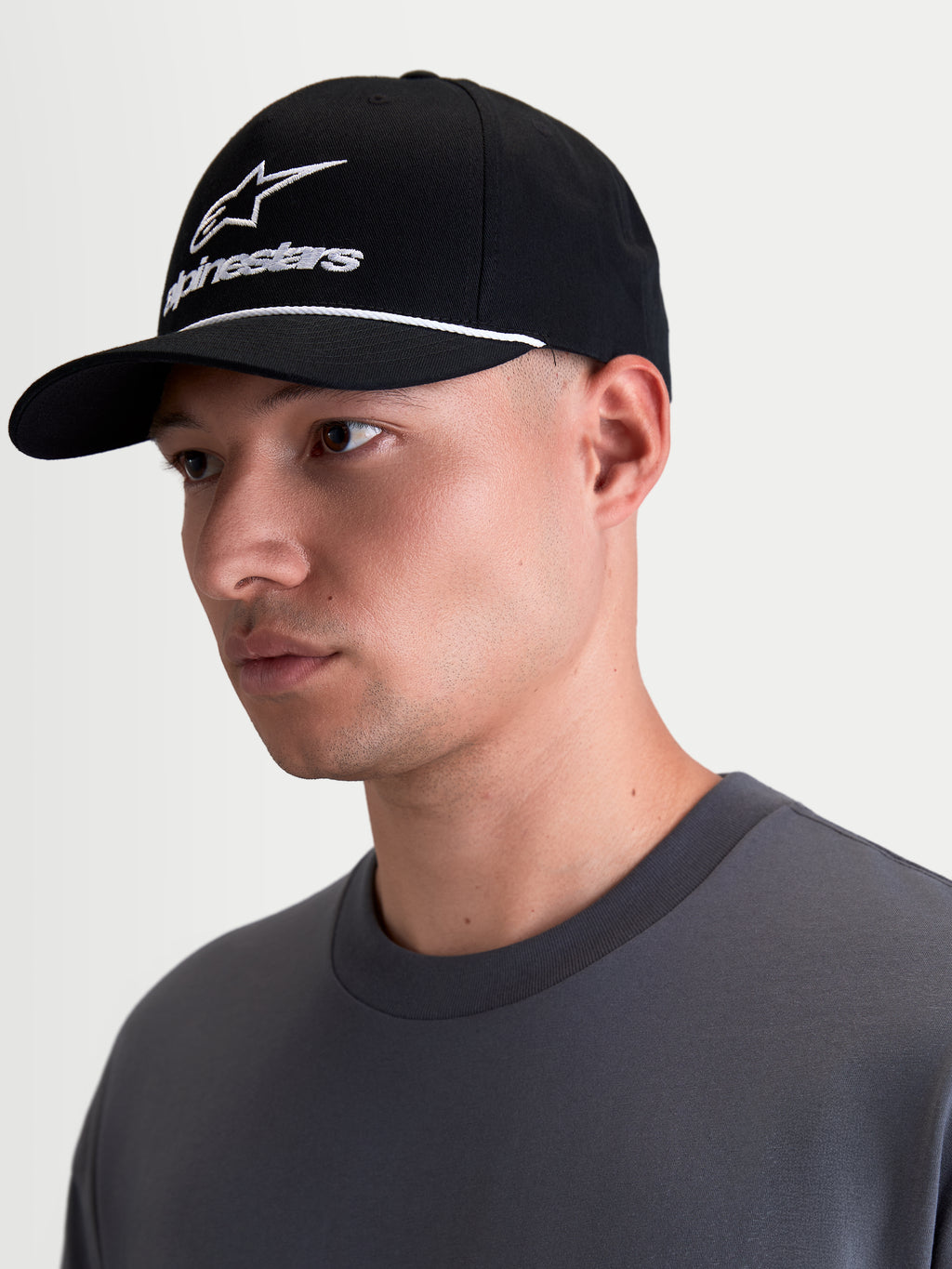 Boné Alpinestars Combo Logo Snapback, boné de sportswear em preto e branco, com pala curva, coroa estruturada, bordado branco do logótipo Astars e detalhe de cordão, mostrado num modelo em vista de perfil.