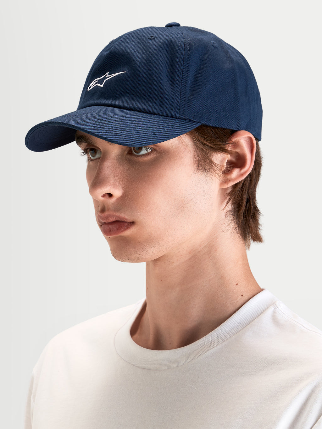 Boné Dylan Dad da Alpinestars, boné de desporto casual em azul-marinho, usado por um modelo, com aba curva, coroa baixa não estruturada e bordado do logótipo Astars branco na frente