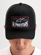 Alpinestars Hemmings Trucker Hat, sportswear snapback cap worn by a model, black, featuring a front woven logo patch and breathable mesh back panels