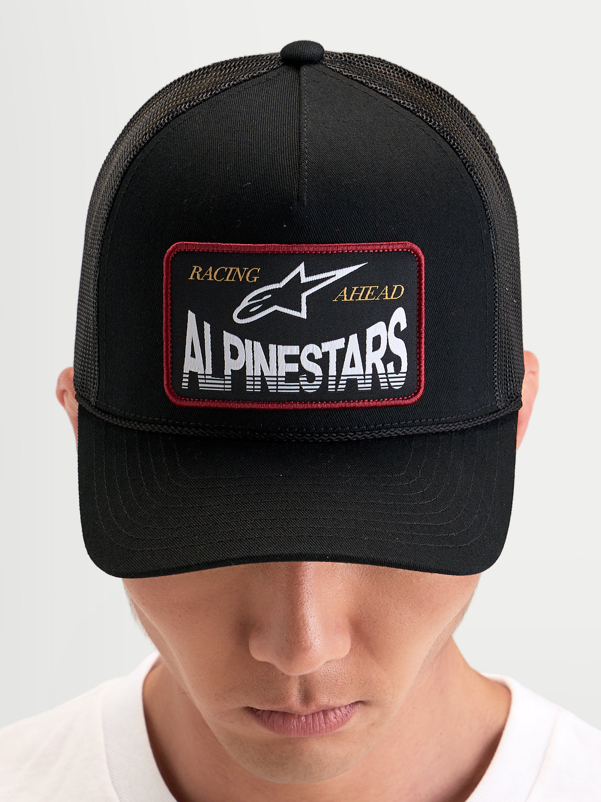 Alpinestars Hemmings Trucker Hat, sportswear snapback cap worn by a model, black, featuring a front woven logo patch and breathable mesh back panels