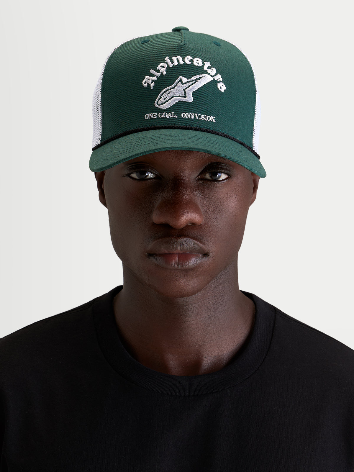 Alpinestars Boné Trucker Baron, boné casual motorsport, verde e branco, aba curva com coroa estruturada e malha traseira, vista frontal num modelo