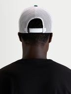 Alpinestars Boné Trucker Baron, boné sportswear casual em malha, vista traseira num modelo a mostrar o fecho snapback ajustável e painéis de malha de poliéster brancos com botão verde na coroa