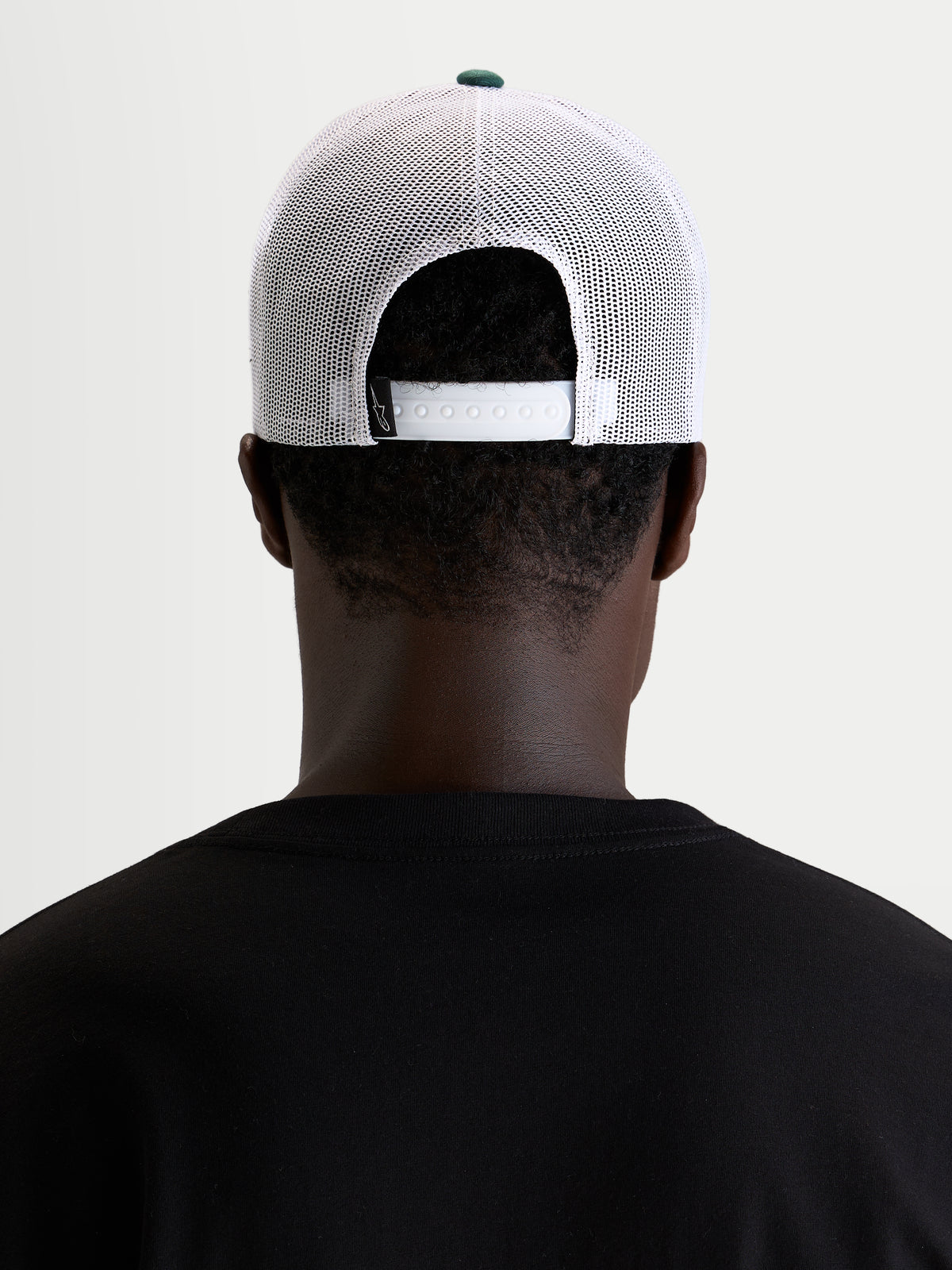 Alpinestars Boné Trucker Baron, boné sportswear casual em malha, vista traseira num modelo a mostrar o fecho snapback ajustável e painéis de malha de poliéster brancos com botão verde na coroa