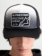Alpinestars Boné Trucker Gravel, boné unissexo de estilo sportswear, preto e branco, com patch tecido Alpinestars Racing Ahead e detalhe de textura de gravilha, copa estruturada e aba curva, vista frontal num modelo.