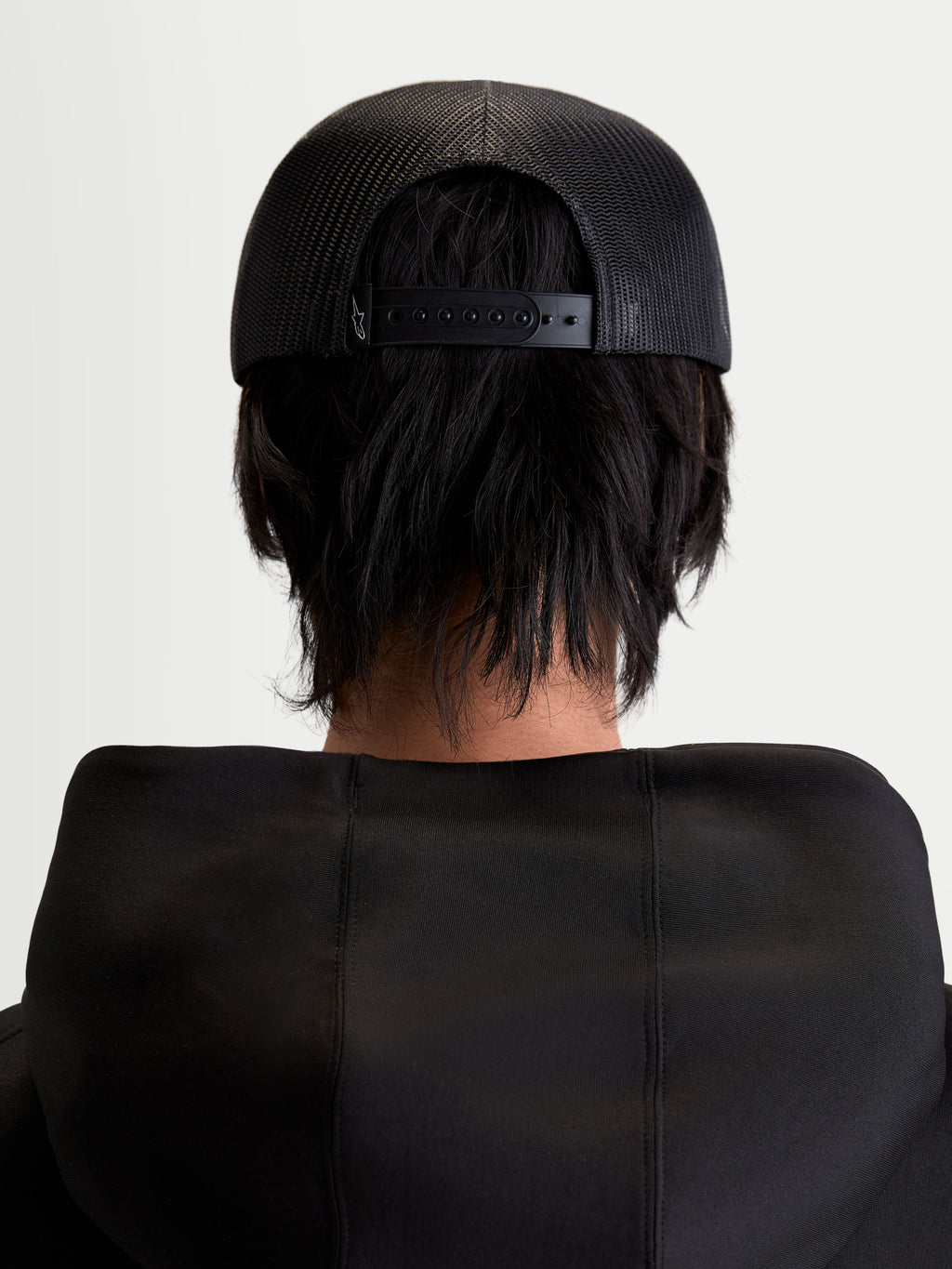 Alpinestars Boné Trucker Gravel, boné unissexo preto, vista traseira em modelo mostrando a malha respirável e o fecho snapback ajustável, sportswear casual.