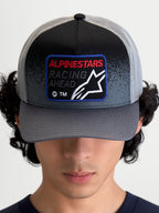 Alpinestars Boné Trucker Gravel, boné de malha de sportswear, cinzento escuro e preto, com pala curva e patch tecido frontal com a inscrição 'Racing Ahead' e o logótipo Astars, vista frontal num modelo.