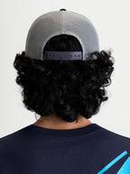 Alpinestars Boné Trucker Gravel, boné sportswear cinzento e preto, vista traseira num modelo mostrando a malha de poliéster respirável e o fecho snapback ajustável para um ajuste personalizado.