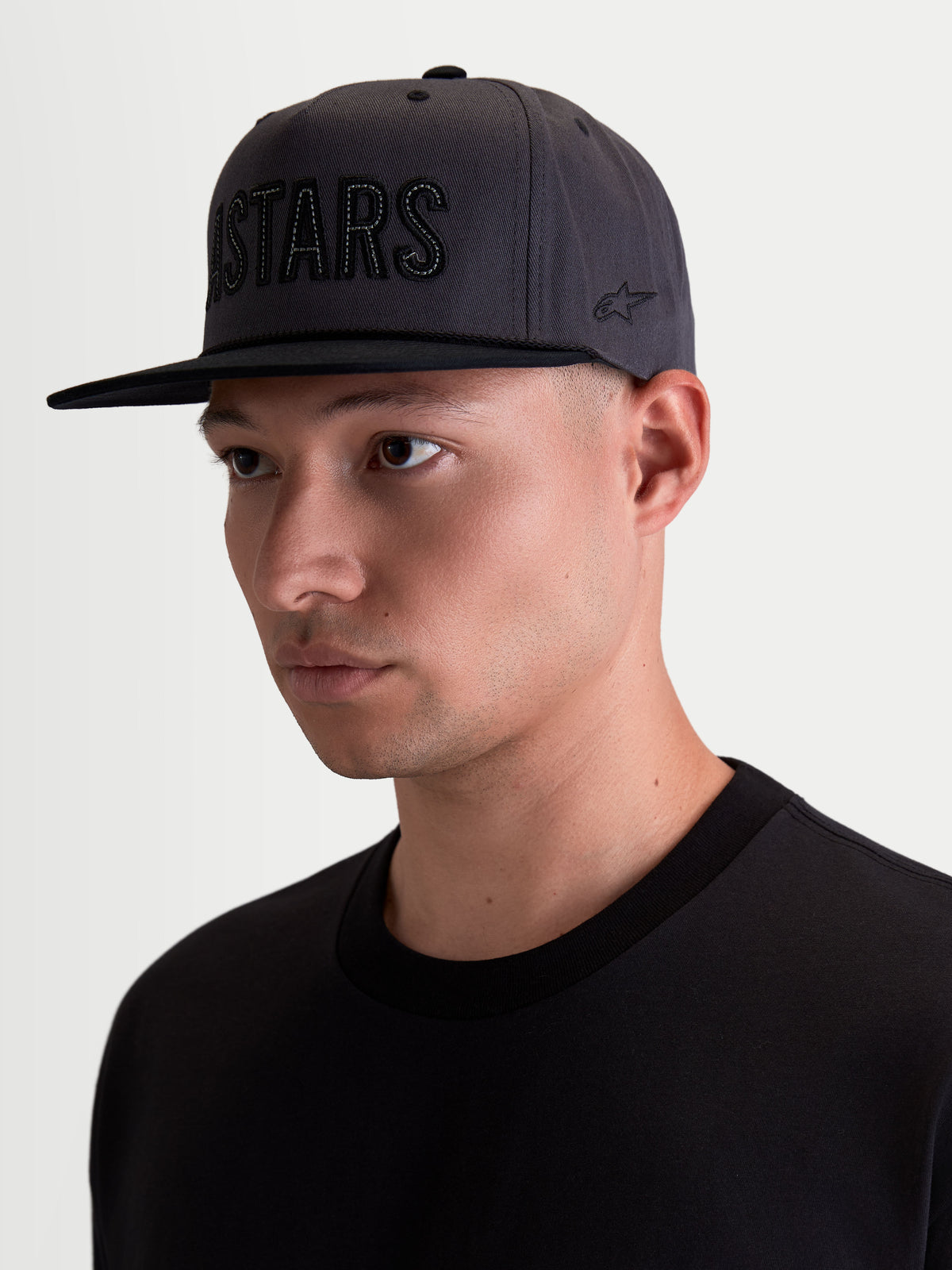 Alpinestars Boné Stadium Snapback, boné de aba plana para homem, cinzento escuro e preto, coroa estruturada, aplique frontal ASTARS e logótipo lateral, em sarja de algodão, vista de modelo.