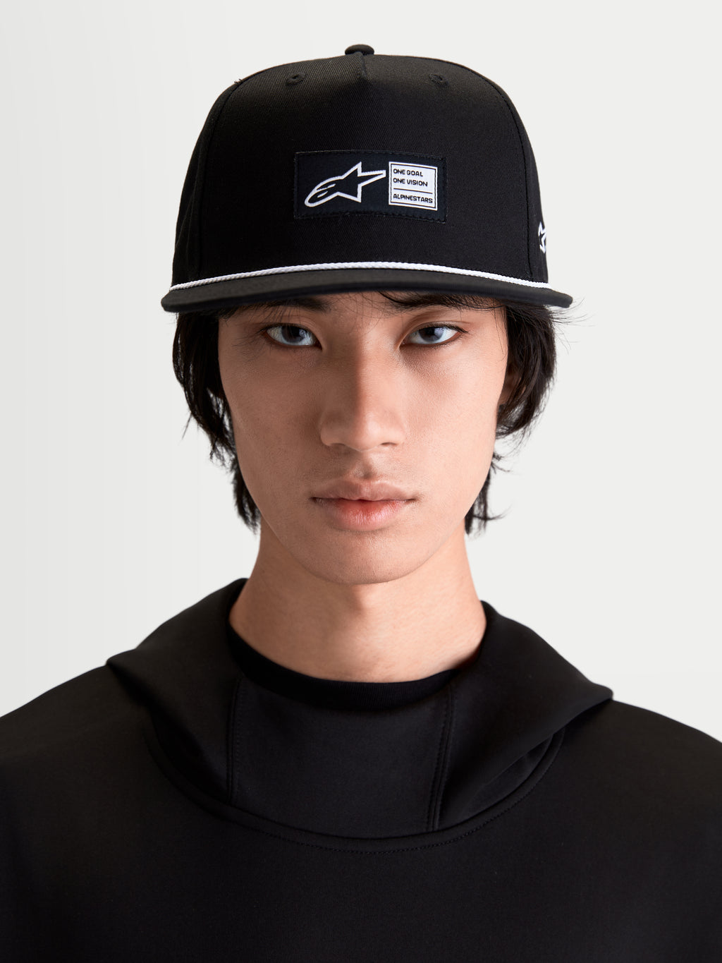 Alpinestars Label Snapback, boné de sportswear preto e branco, aba plana com detalhe de corda branca, etiqueta frontal tecida, sarja de algodão, visto no modelo.