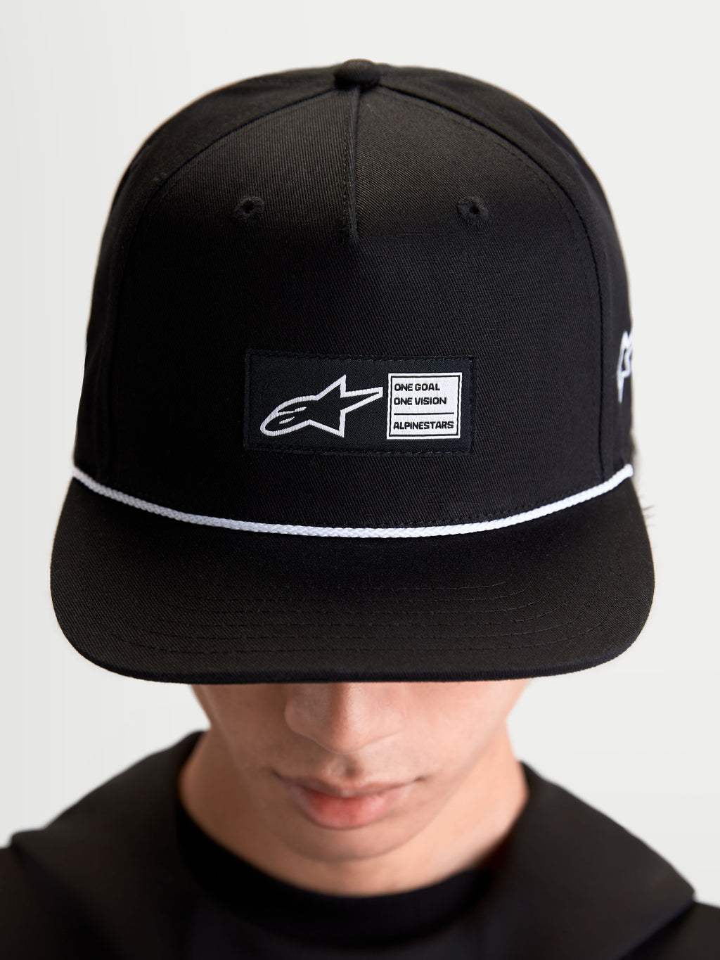 Alpinestars boné Label Snapback, acessório sportswear lifestyle unissexo, preto e branco, em sarja de algodão, com copa estruturada, aba plana, detalhe de cordão branco e etiqueta tecida frontal com branding Alpinestars, mostrado no modelo.