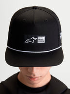 Alpinestars boné Label Snapback, acessório sportswear lifestyle unissexo, preto e branco, em sarja de algodão, com copa estruturada, aba plana, detalhe de cordão branco e etiqueta tecida frontal com branding Alpinestars, mostrado no modelo.