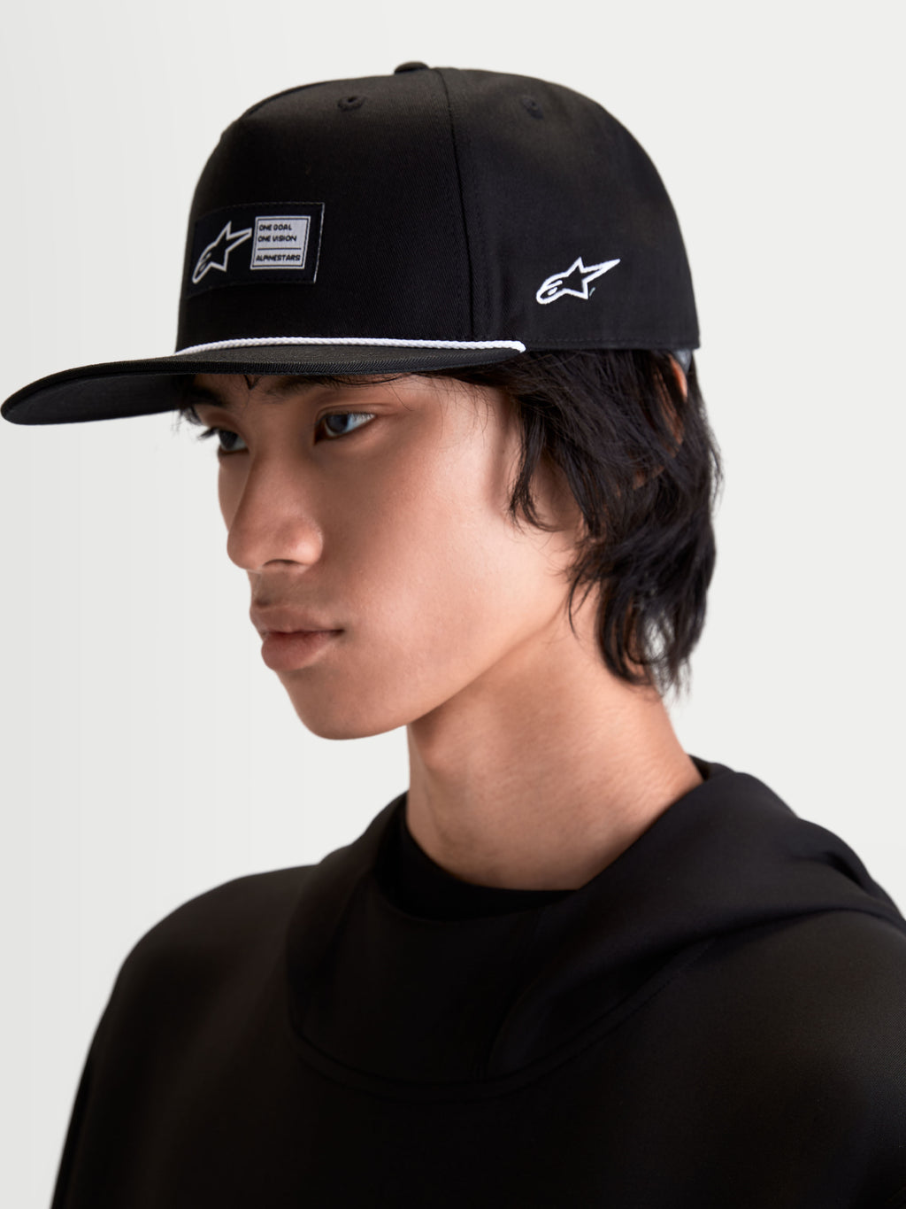 Alpinestars Boné Label Snapback, boné sportswear de aba plana e copa estruturada, preto com cordão branco e etiqueta tecida frontal, logótipo bordado na lateral, mostrado em modelo para um estilo lifestyle inspirado no desporto motorizado.