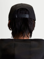 Boné Alpinestars Label Snapback, boné de sportswear preto unissexo, vista traseira num modelo com fecho snapback ajustável e pequeno logótipo branco, construção estruturada em sarja de algodão.