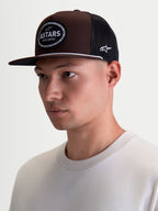 Alpinestars Boné Trucker Hotlink, boné de sportswear em modelo, castanho e preto, com aba plana e copa estruturada em sarja, patch frontal com logótipo Astars e rebordo em corrente de bicicleta.