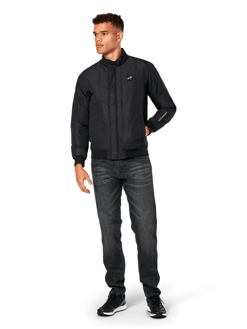 Alpinestars Precedent Jacket, Quilted Sportswear Jacket, Black, worn with dark grey jeans and black sneakers, featuring an angled quilt pattern, low track collar, rib-knit cuffs and hem, with a white logo patch on the chest and sleeve embroidery.