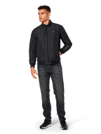 Alpinestars Precedent Jacket, Quilted Sportswear Jacket, Black, worn with dark grey jeans and black sneakers, featuring an angled quilt pattern, low track collar, rib-knit cuffs and hem, with a white logo patch on the chest and sleeve embroidery.