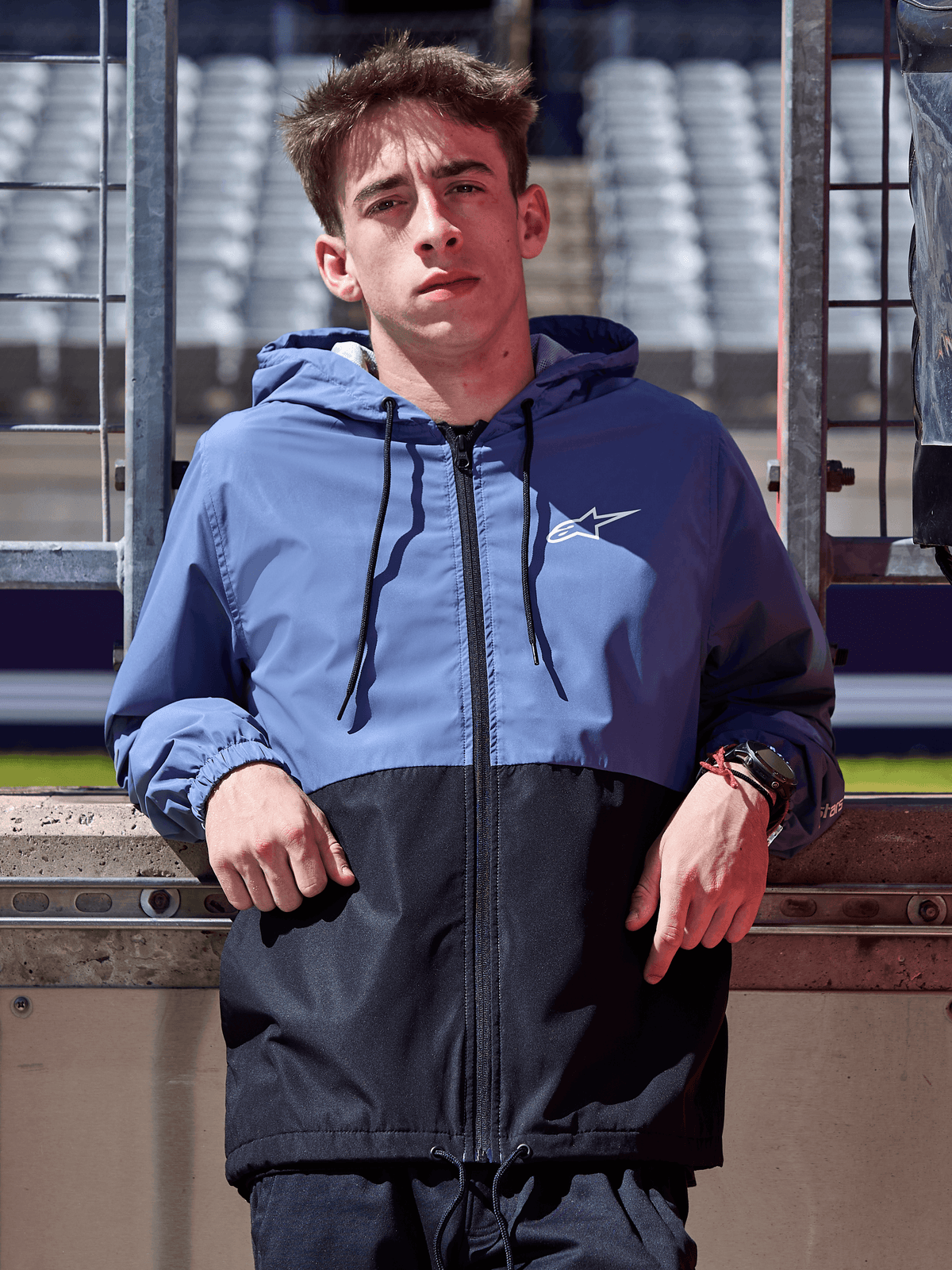 Alpinestars Speeder Windbreaker Jacket, azul ardósia e preto, casaco corta-vento com capuz e design de corpo bloqueado, logótipo branco no peito, vestuário casual de estilo de vida usado numa pista de corridas
