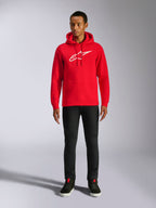 Alpinestars Ageless V3 Hoodie, streetwear casual, vermelho com logótipo Alpinestars bordado a branco, vestido por um modelo masculino com calças pretas, capuz com cordão, bolso canguru frontal, design moderno inspirado no desporto motorizado