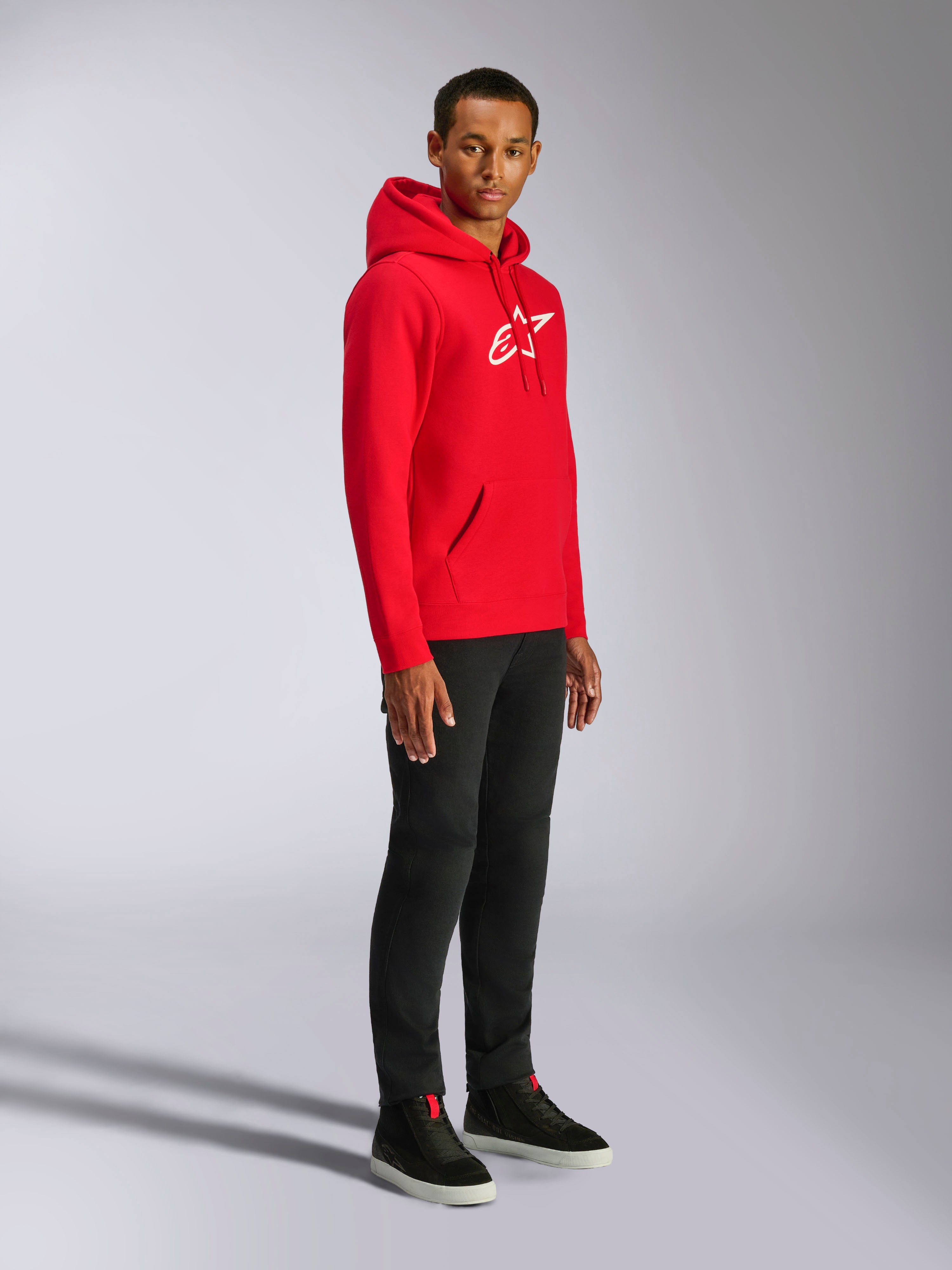 Alpinestars Ageless V3 Hoodie, vermelho com logótipo bordado a branco, hoodie casual de sportswear usado por um homem com calças pretas e sapatilhas pretas, com capuz de cordão e punhos canelados