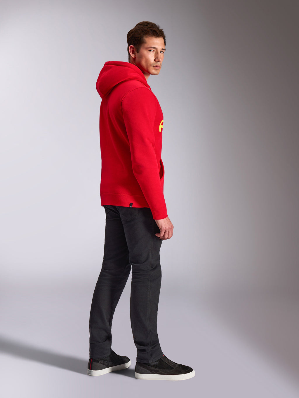 Alpinestars Linear Wordmark V3 Hoodie, Red, casual streetwear, model viewed from the side and back wearing a red pullover hoodie with yellow branding, dark grey jeans, and black sneakers, studio lifestyle shot