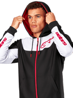 Alpinestars Sessions V3 Hoodie, Black White and Red, zip-front hoodie worn by a man with the hood up, featuring red Alpinestars logos on the chest and sleeves, casual motorsport streetwear
