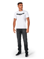 Alpinestars Elliptic CSF Tee, t-shirt de manga curta, branca, logótipo Astars arqueado a preto com símbolo de estrela cor de laranja, usada por modelo com calças de ganga pretas e ténis, streetwear casual de desportos motorizados