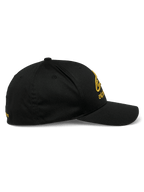 Alpinestars Gild Hat, boné sportswear, preto e dourado, vista de perfil lateral com aba curva, coroa estruturada e bordado metálico 3D dourado na frente e na lateral, tecido em sarja elástica