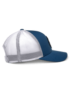 Boné Trucker Alpinestars Gambit, azul e branco, vista de perfil, aba curva com coroa estruturada, painéis frontais em sarja azul e malha de poliéster branca na parte de trás, acessório casual inspirado no desporto motorizado