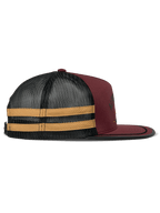 Boné Trucker Alpinestars Backline, vermelho tijolo, preto e mostarda, vista de perfil lateral, frente em sarja vermelho escuro com malha preta na parte posterior e riscas amarelas laterais, pala plana com acabamento em passamanaria preta, acessório casual inspirado no desporto motorizado