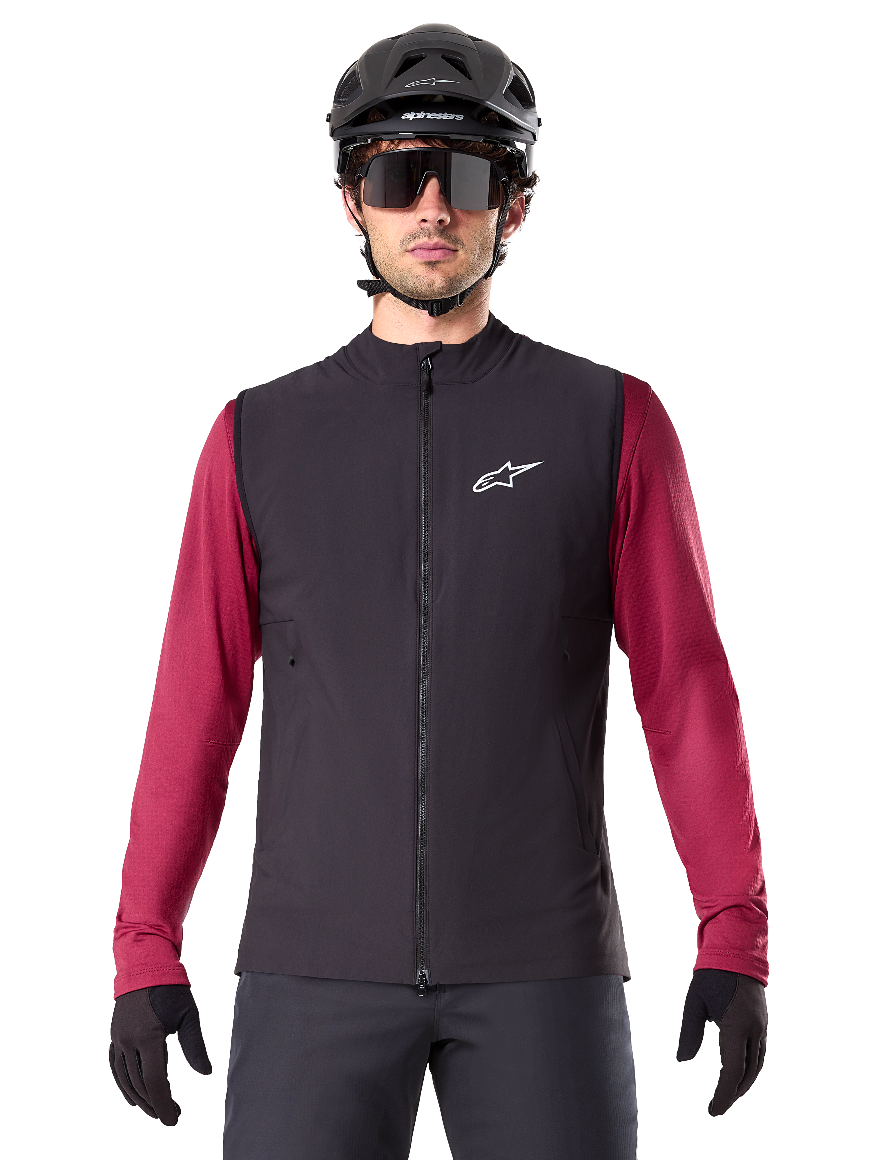 Alpinestars A-Dura Thermal Vest, Black insulated cycling vest, worn by a model with a maroon long-sleeve jersey, black MTB helmet, and sunglasses, featuring a white logo on the chest, lightweight thermal protection for mountain biking