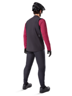 Alpinestars A-Dura Thermal Vest, Black cycling vest, shown from the back on a model wearing a maroon long-sleeve jersey and black cycling pants, paired with a black mountain bike helmet and gloves, technical gear for cold-weather riding