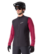 Alpinestars A-Dura Thermal Vest, Black, Cycling Thermal Gilet, worn over a maroon long-sleeve shirt, featuring a white chest logo, paired with a black MTB helmet and sunglasses, insulated performance layer for mountain biking