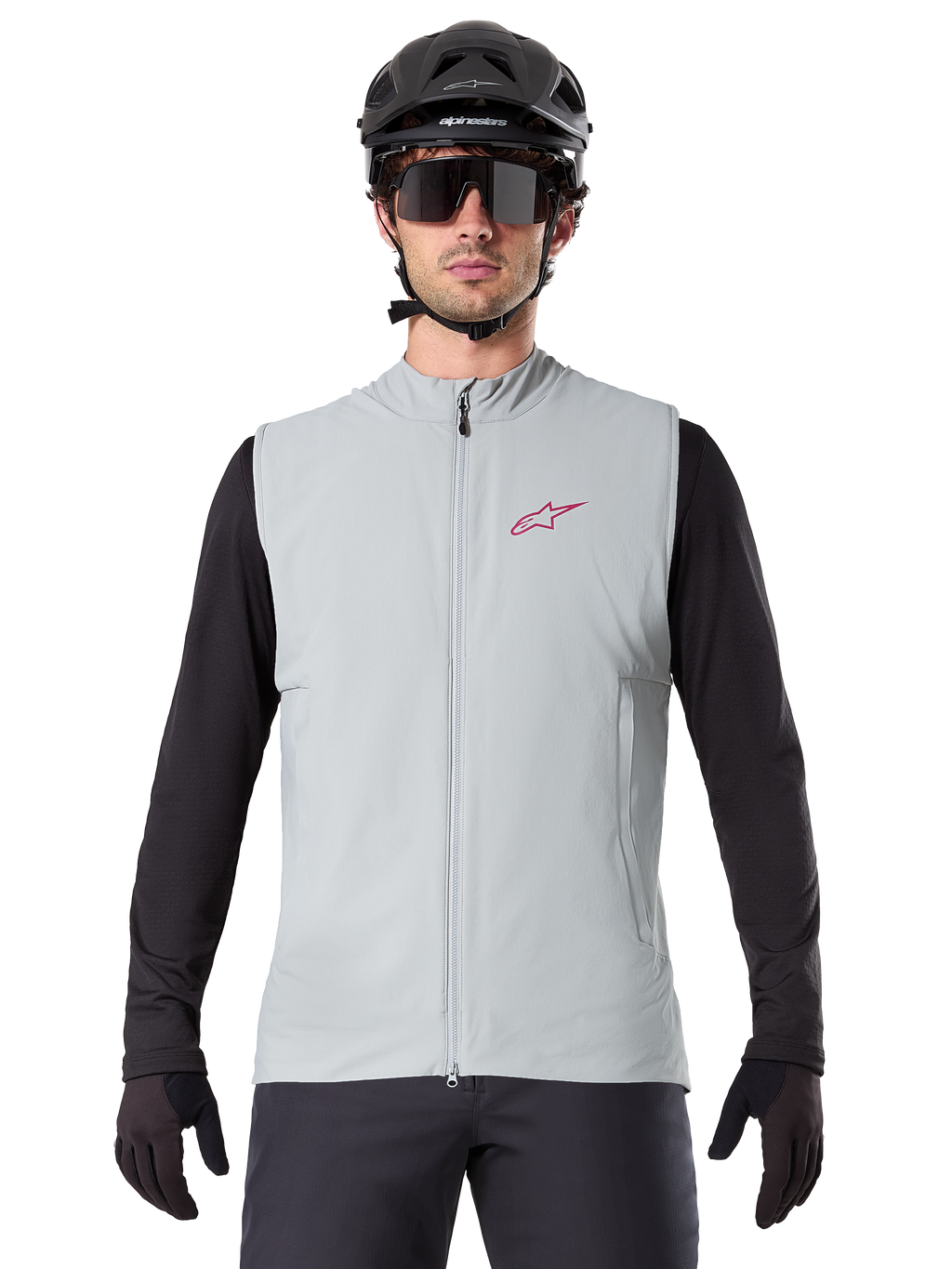 Colete Térmico Alpinestars A-Dura, colete de ciclismo, cinzento titanium, usado com uma camisola de manga comprida preta e capacete de ciclismo preto, logótipo da estrela Alpinestars vermelho no peito, leve e isolado para mountain biking.