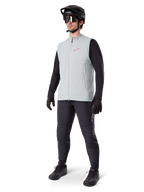 Alpinestars Colete Térmico A-Dura, colete de ciclismo cinzento titânio com logótipo cor-de-rosa, usado por um modelo com camisola de manga comprida preta, calças cinzento-escuras e capacete de BTT preto, equipamento de performance para climas frios