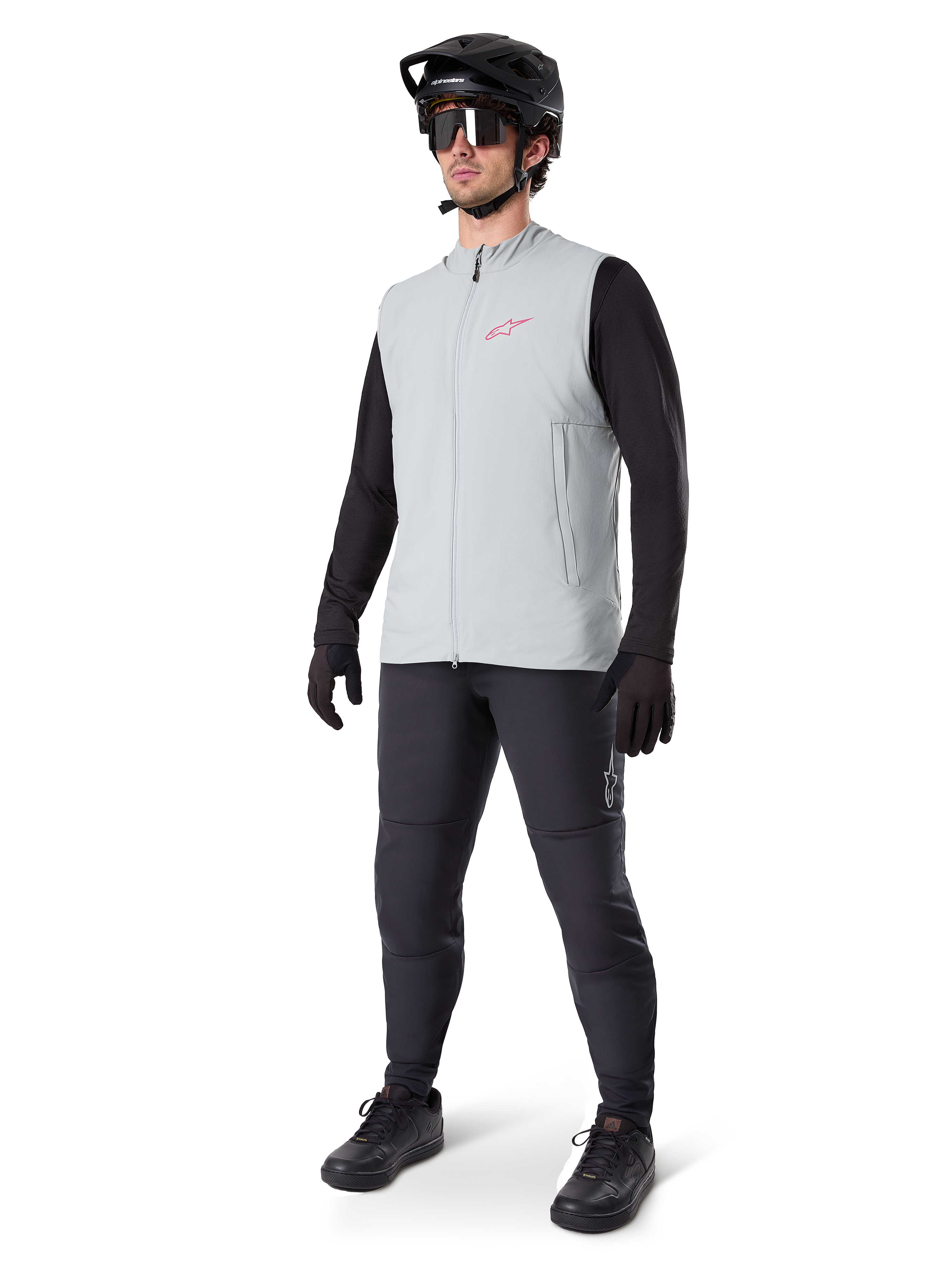 Alpinestars Colete Térmico A-Dura, colete de ciclismo cinzento titânio com logótipo cor-de-rosa, usado por um modelo com camisola de manga comprida preta, calças cinzento-escuras e capacete de BTT preto, equipamento de performance para climas frios