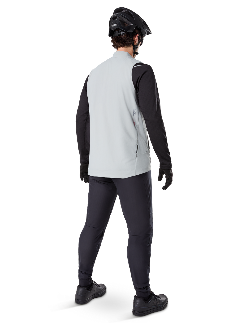 Alpinestars Colete Térmico A-Dura, Cinza Titanium, vista traseira de modelo a usar o colete de ciclismo com isolamento sobre uma camisola de manga comprida preta e calças escuras, com capacete de BTT e luvas pretas, concebido para ciclismo fora de estrada em climas frios